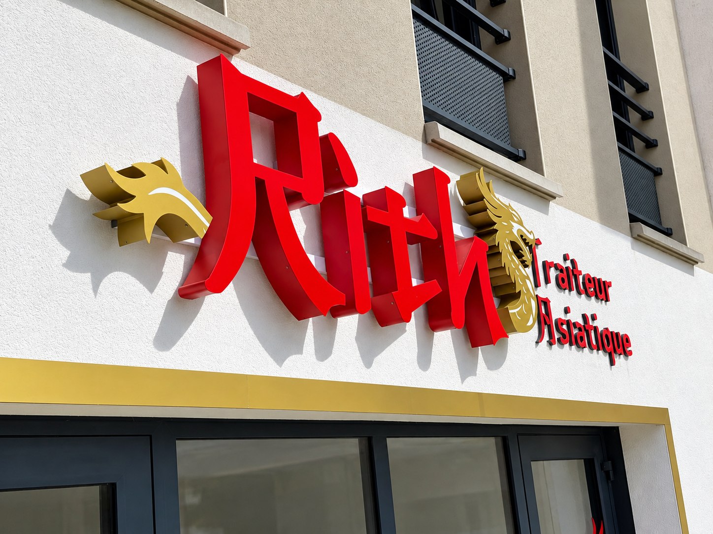 Enseigne rouge Rith Traiteur Asiatique et dragons dorés en relief sur une façade claire