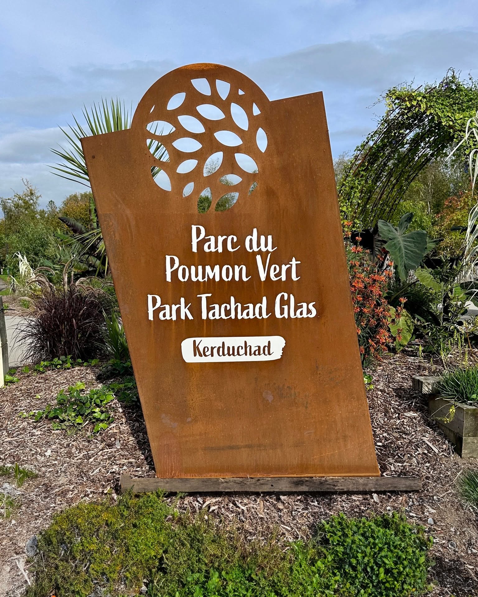 Totem d’entrée du Parc du Poumon Vert, avec décor végétal découpé et texte bilingue.