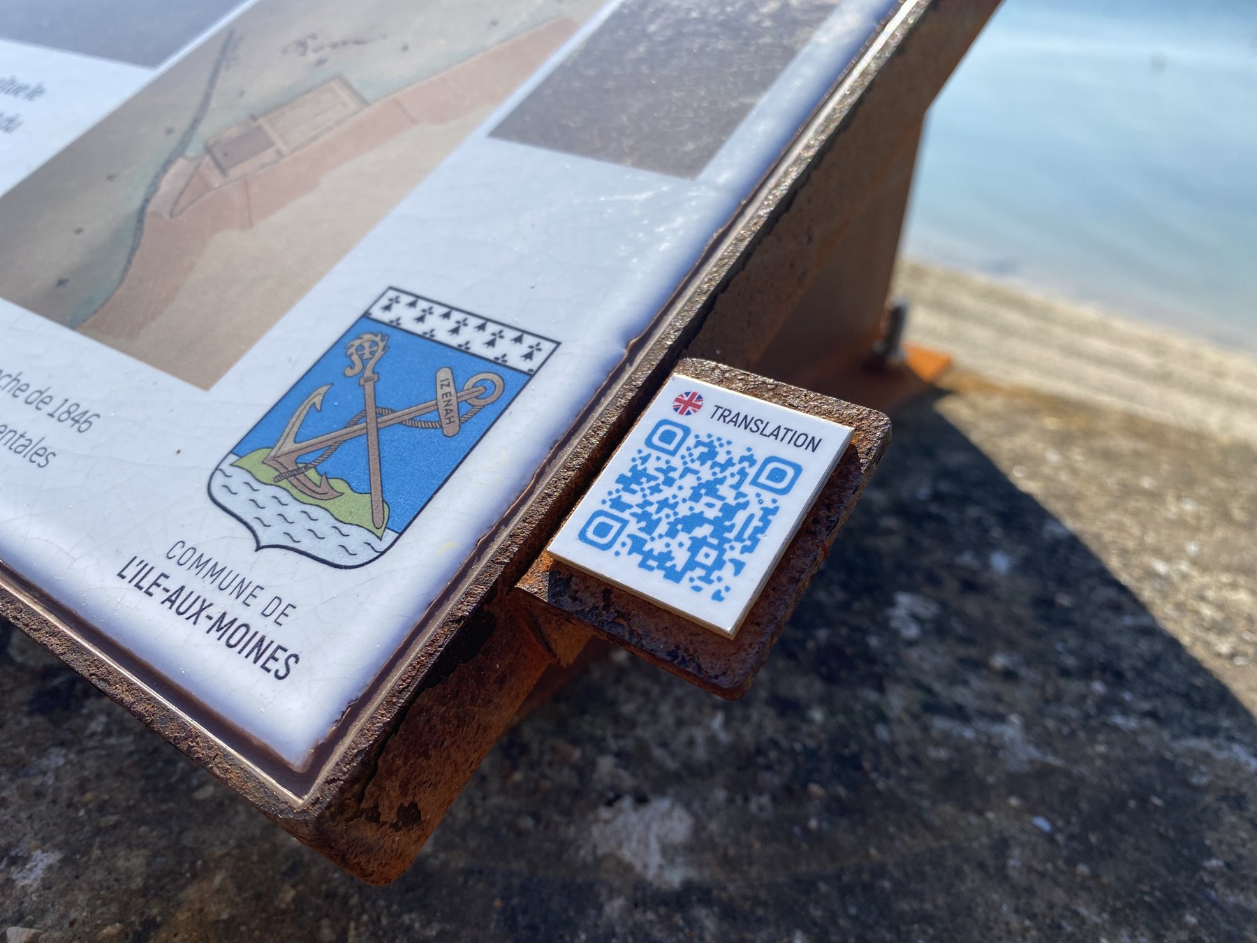 Détail d’un panneau en lave émaillée à Plozévet avec blason et QR code.