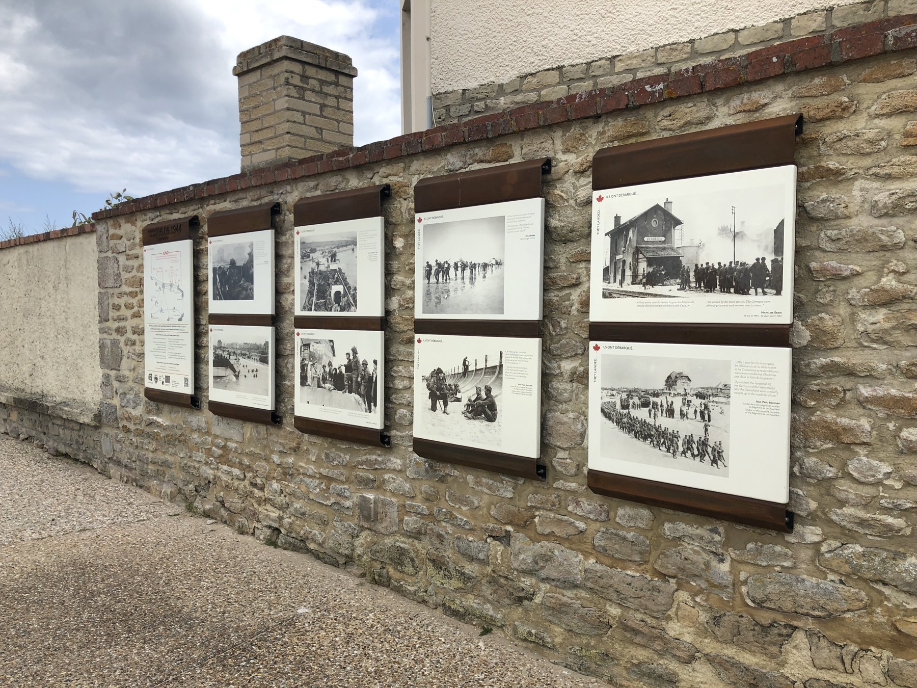 Ensemble de plaques avec photographies d’archives sur un mur à Bernières-sur-Mer.