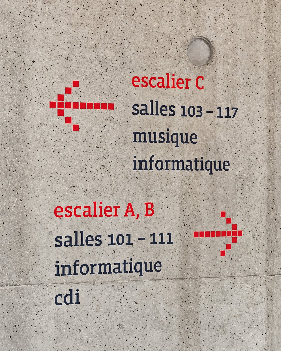 Flèches rouges et indications des escaliers et salles appliquées directement sur un mur en béton
