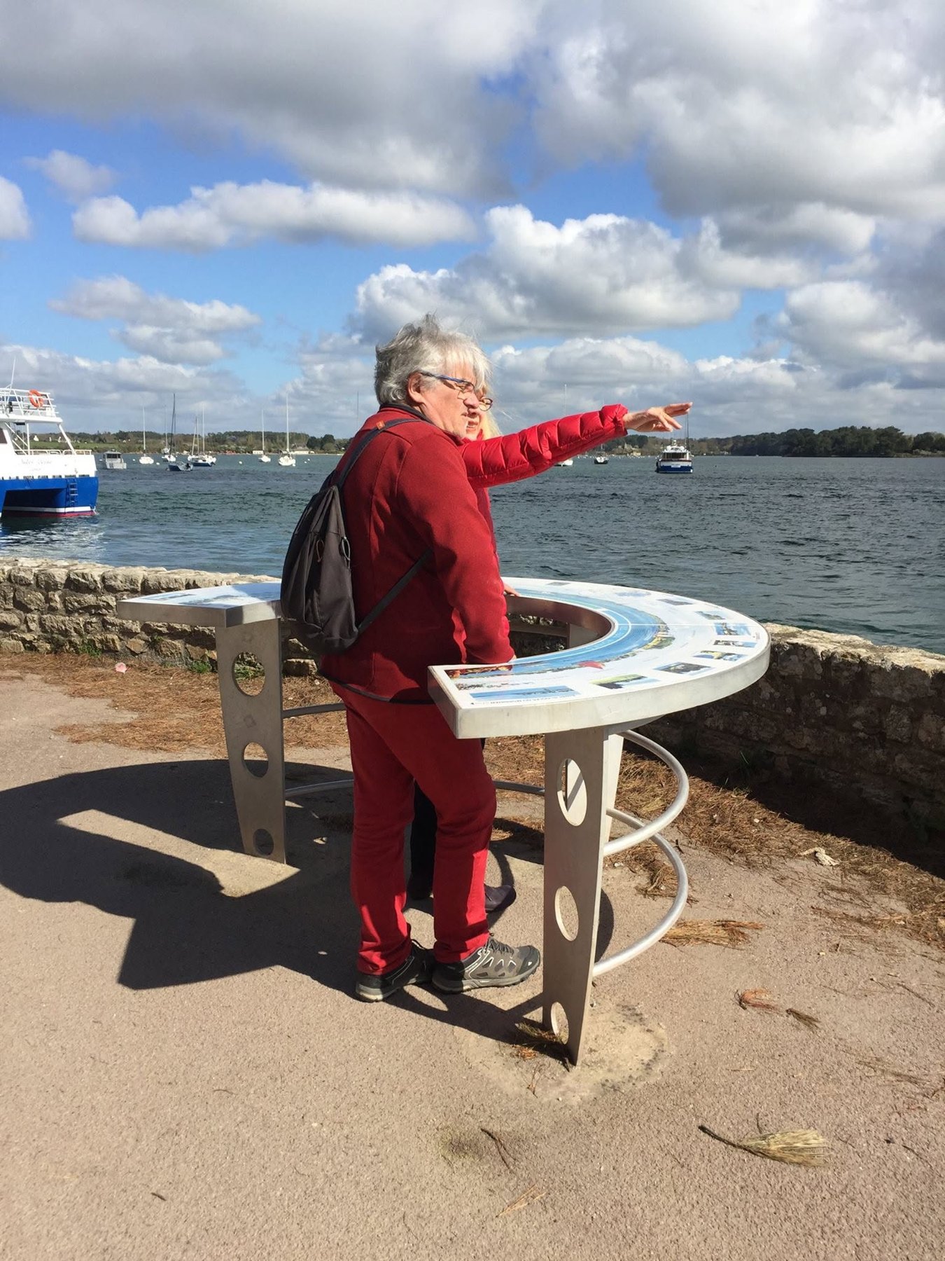 Visiteuse lisant une table d’orientation circulaire face à un paysage maritime.